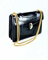 Sac à bandoulière noir en cuir lisse avec chaîne dorée et fermoir tête de serpent